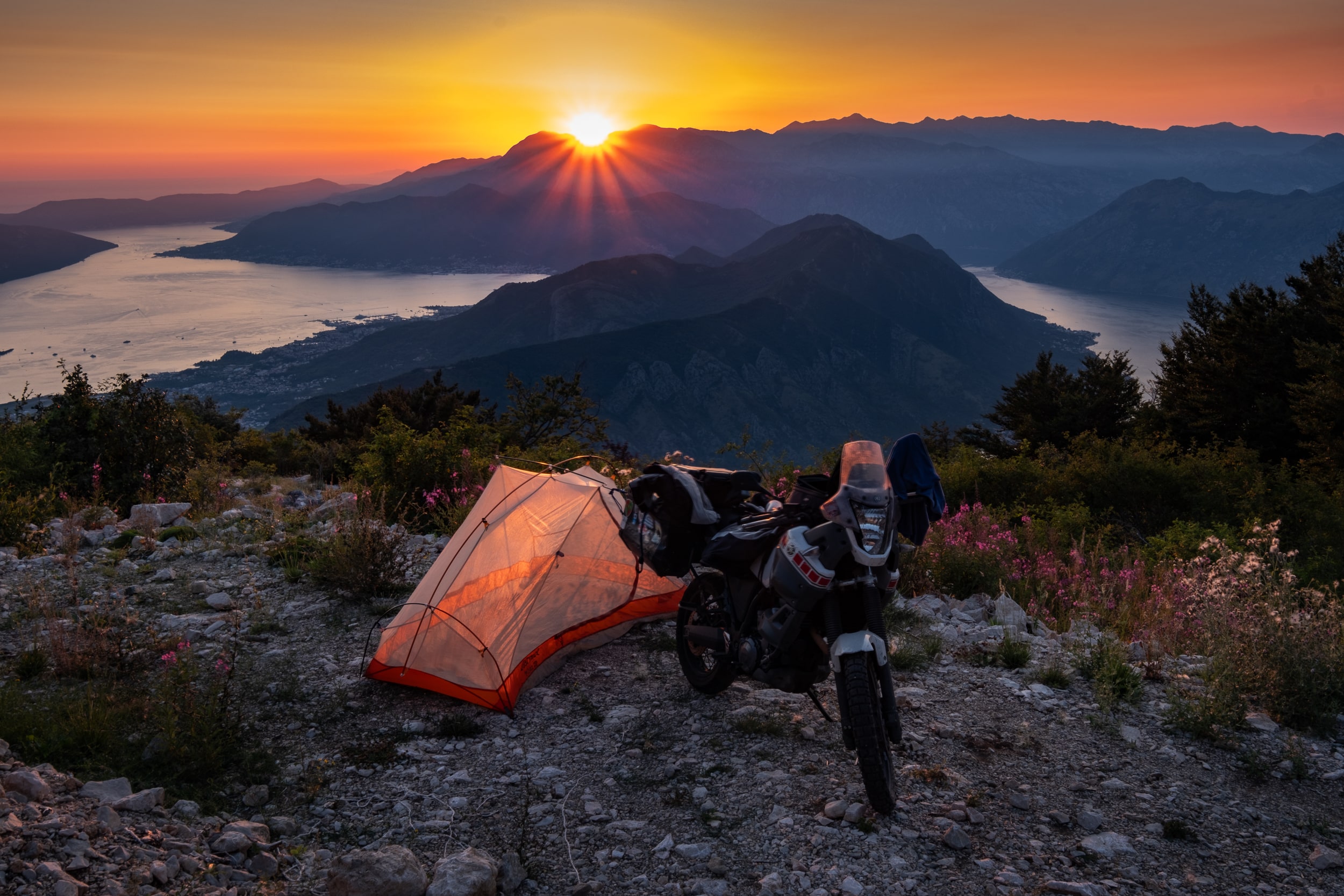 motorcycle next to a tent high above a bay at sunset
