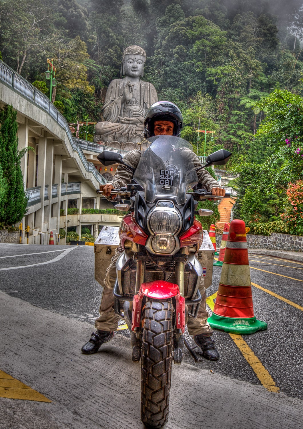 rider on a motorcycle with thick jungle and Buddha's statue behind