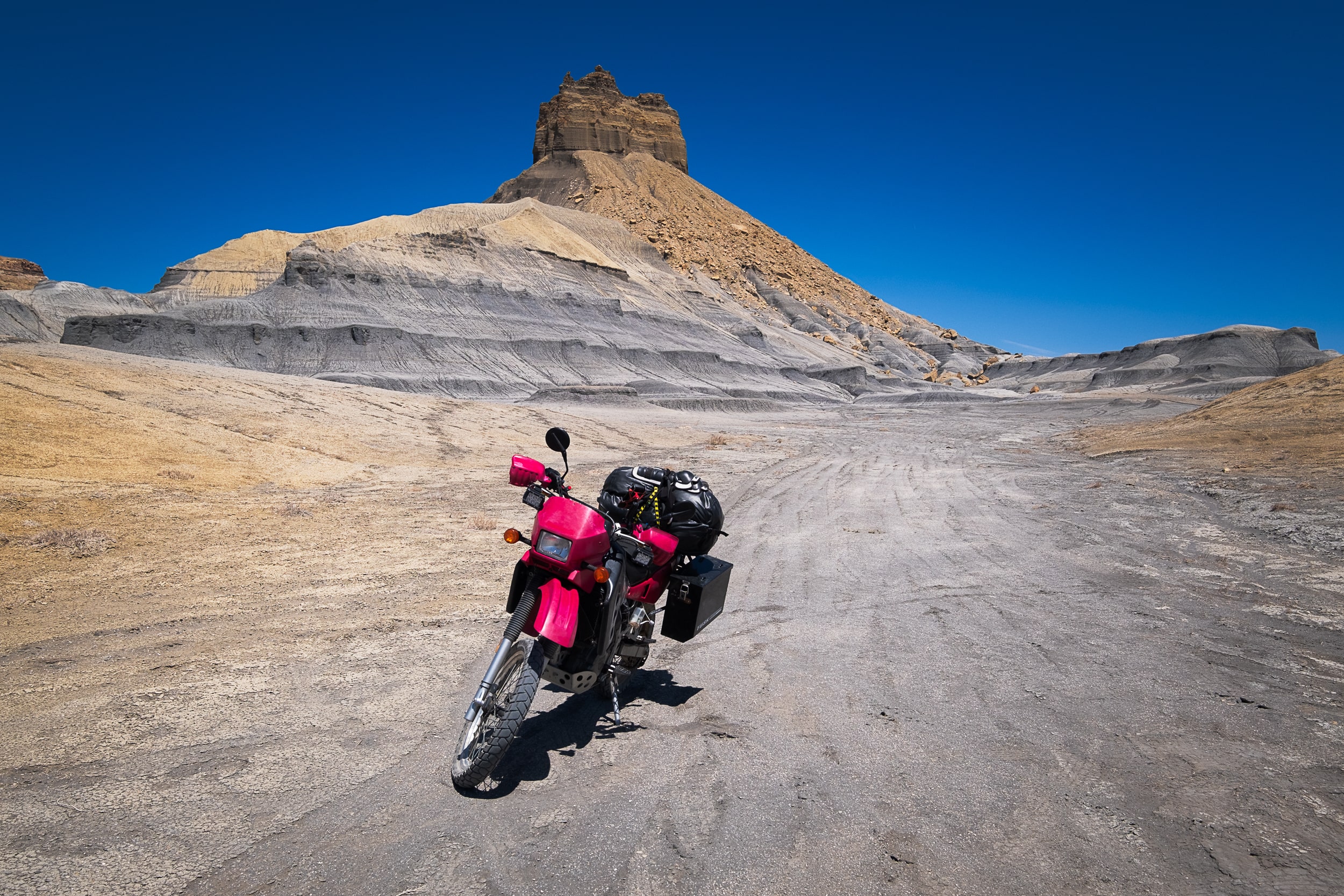 motorcycle parked on a dirt road with desert cliffs behind