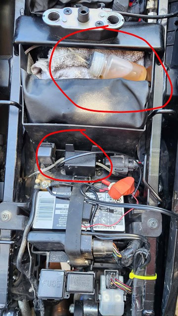 motorcycle underseat area with a blxk box and oil filled bottle